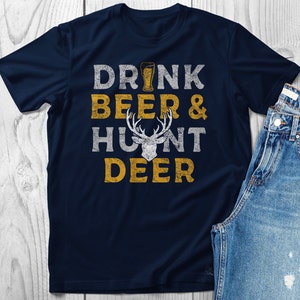 May include: A navy blue t-shirt with a distressed graphic design that reads "Drink Beer & Hunt Deer". The graphic includes a beer glass and a deer head.