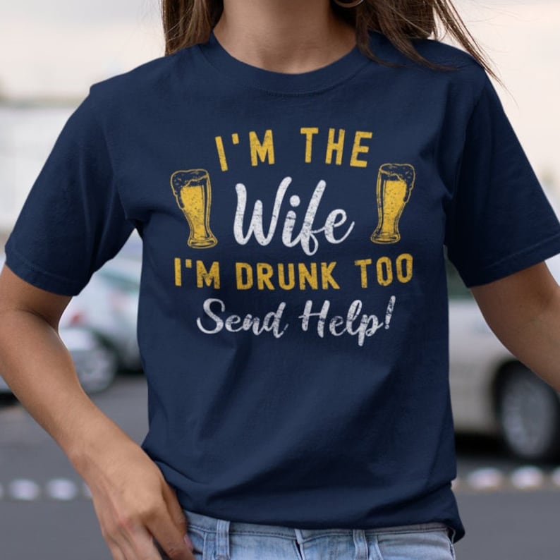 May include: A navy blue t-shirt with a distressed white graphic that reads "I'm the Wife I'm Drunk Too Send Help!" with two yellow beer mugs on either side of the text.