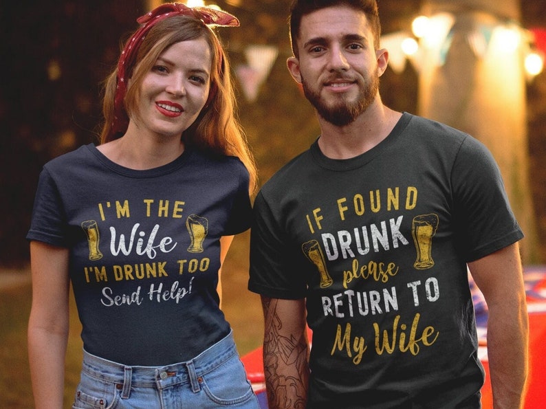 May include: A couple wearing matching navy blue and black t-shirts with a beer-themed design. The woman's shirt says "I'm the Wife I'm Drunk Too Send Help!" and the man's shirt says "If Found Drunk Please Return To My Wife".