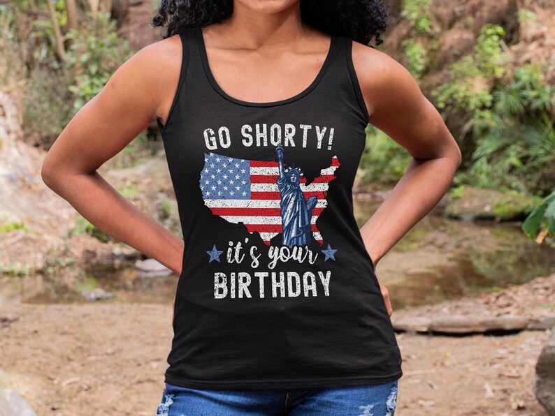 Puede incluir: Camiseta de tirantes negra con un dise&ntilde;o de bandera estadounidense desgastado y el texto "Go Shorty! It's your Birthday" con una estrella a cada lado del texto.
