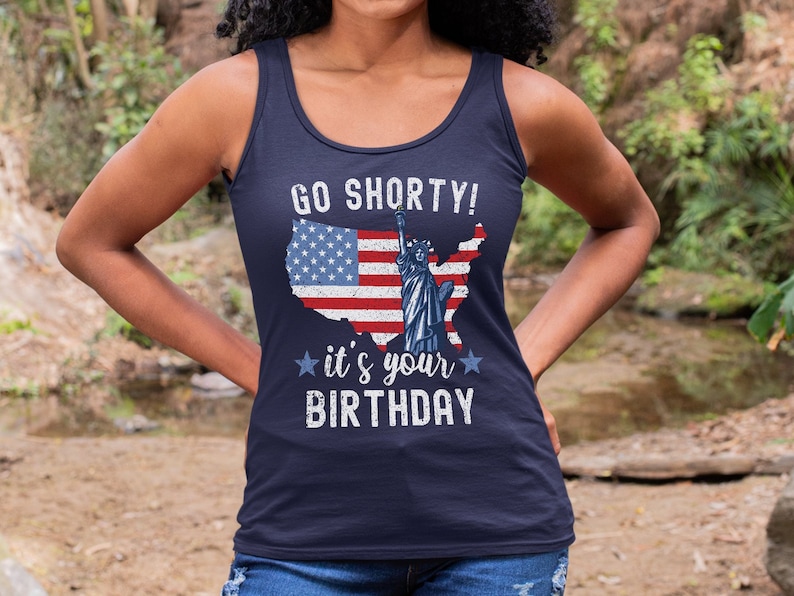 Puede incluir: Un top de tirantes azul marino con un dise&ntilde;o de bandera estadounidense desgastado y el texto "GO SHORTY! it's your BIRTHDAY".