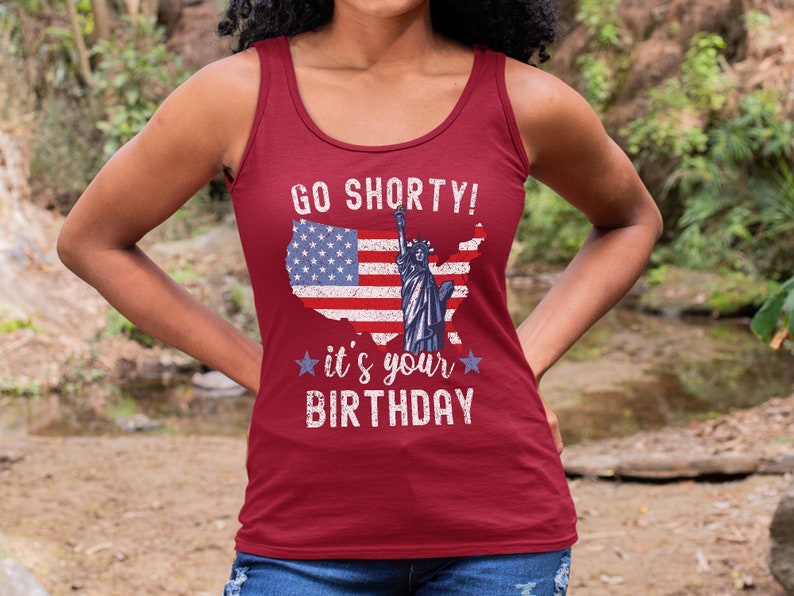 Puede incluir: Camiseta de tirantes roja con un dise&ntilde;o de bandera estadounidense desgastado y el texto "Go Shorty! It's your Birthday" en blanco.