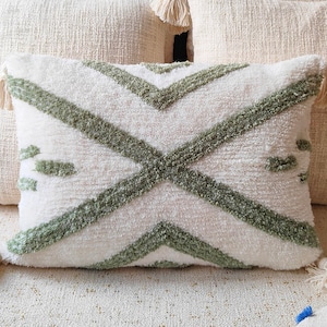 May include: A white throw pillow with a green geometric pattern. The pillow has a fringe trim and is sitting on a white couch.