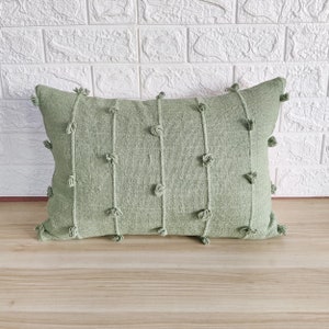 May include: A sage green throw pillow with a textured fabric and small pom-poms around the edges.
