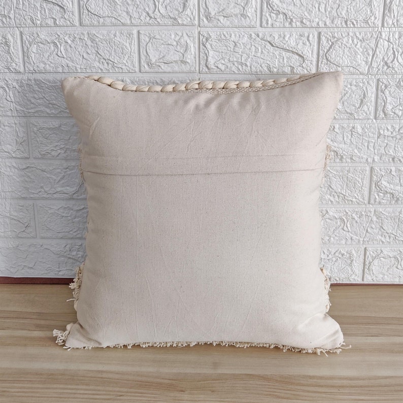 May include: A cream-colored throw pillow with a fringe border. The pillow is made of a soft, woven fabric and has a zipper closure.