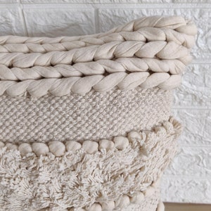 May include: A cream-colored throw pillow with a braided top, a textured middle section, and a fluffy, fringed bottom.