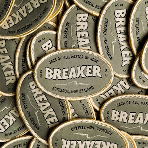 May include: An assortment of olive green oval patches with the word "BREAKER" in white block letters. Each patch has a gold border and the text "JACK OF ALL, MASTER OF NONE" and "AOTEAROA, NEW ZEALAND".