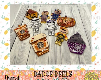 May include: A set of 10 Halloween-themed resin badge reels featuring a variety of designs, including a pumpkin spice latte, a mummy, a scarecrow, a pumpkin, a cupcake, and a gingerbread man. The badge reels are all decorated with glitter and other embellishments.