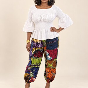 May include: A white long-sleeved blouse with a smocked bodice and flared sleeves paired with loose-fitting trousers featuring a vibrant, multi-colored patchwork pattern of various geometric and floral prints in shades of red, blue, green, and orange.