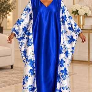 May include: A floor-length kaftan dress featuring a solid royal blue center panel and contrasting white side panels with a vibrant blue floral print. The garment has a V-neckline and loose, flowing sleeves with gathered elasticized cuffs.