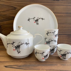 Puede incluir: Un juego de té de porcelana blanca con un diseño de bambú. El juego incluye una tetera, cuatro tazas de té y una bandeja de servir.