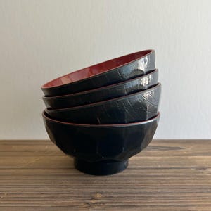 May include: A stack of four black lacquer bowls with a textured surface. The interior of each bowl is red, creating a striking contrast. The bowls are stacked on top of each other, showcasing their shape and design.