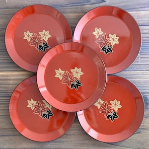May include: Set of five red lacquer plates with a gold and black maple leaf design. The plates are round and have a raised rim.