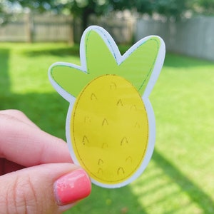 May include: A yellow pineapple sticker with green leaves. The sticker has a glossy finish and is perfect for adding a touch of tropical fun to any project.