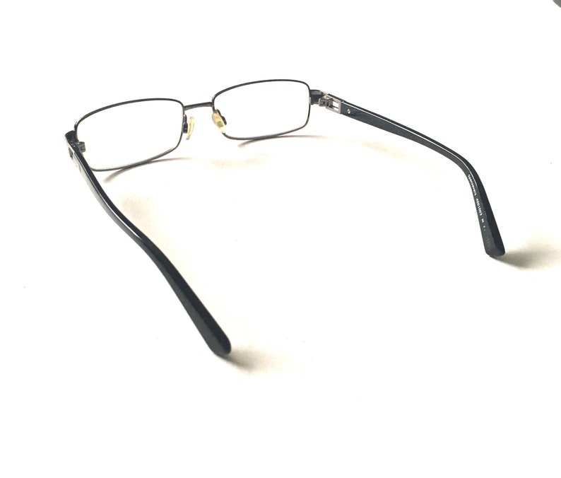 May include: Black metal frame eyeglasses with clear lenses. The glasses are shown from the back, with the arms extending out to the sides.