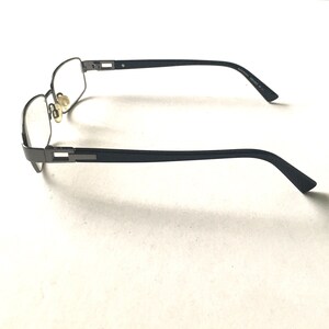 May include: A pair of black metal eyeglasses with clear lenses. The glasses have a rectangular frame and are in a side view.