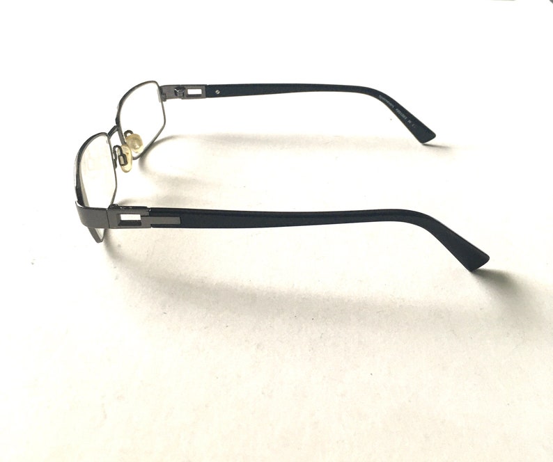May include: A pair of black metal eyeglasses with clear lenses. The glasses have a rectangular frame and are in a side view.