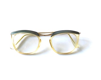 May include: A pair of vintage eyeglasses with a gold metal frame and clear lenses. The top of the frame is a dark green plastic.