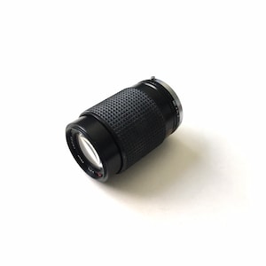 May include: A black camera lens with a silver ring around the front. The lens has a textured surface and a small red dot on the side.