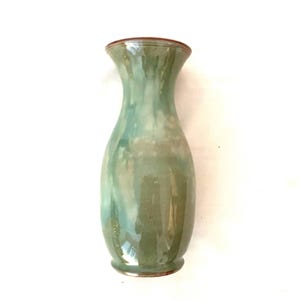 May include: A handcrafted ceramic vase with a glossy, mottled green and blue glaze. The vase has a slender neck and a slightly flared rim with a brown accent. The base also has a brown accent. The vase is approximately 20 cm tall.
