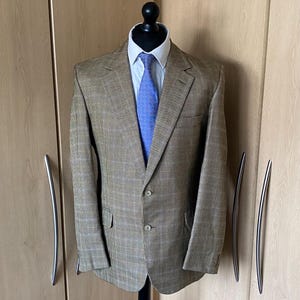 Könnte beinhalten: Ein brauner und beigefarbener karierter Blazer mit einer blauen gemusterten Krawatte. Der Blazer hat einen Knopfverschluss und zwei Taschen.