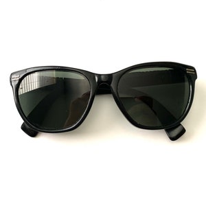 Może przedstawiać: Czarne okulary przeciwsłoneczne z oprawką typu "kocie oko" i ciemnymi szkłami.