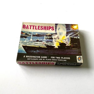 May include: A vintage Battleships board game box with a colorful illustration of a naval battle scene. The box features the text "Battleships" in bold pink letters and the words "A Waddington Game for Two Players" in black text.