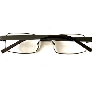 May include: Dark gray rectangular eyeglasses with clear lenses. The glasses have a thin, dark gray frame and temples. The design is modern and minimalist, suitable for everyday wear.