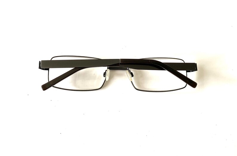 May include: Dark gray rectangular eyeglasses with clear lenses. The glasses have a thin, dark gray frame and temples. The design is modern and minimalist, suitable for everyday wear.