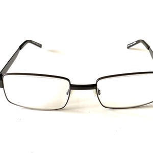 May include: Rectangular eyeglasses with a black metal frame. The lenses are clear, and the arms are thin and extend to the temples. The glasses are set against a white background.