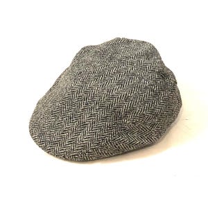 Pode incluir: Um boné de tweed cinza e preto com padrão de espinha de peixe.