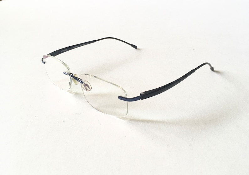 May include: A pair of black rimless glasses with clear lenses. The glasses have a thin, black frame and are designed for everyday wear.
