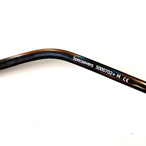 May include: Close-up of a glasses arm with a dark brown and blue marbled pattern. The text "Specsavers 5000702+ M CE" is printed in white on the arm.