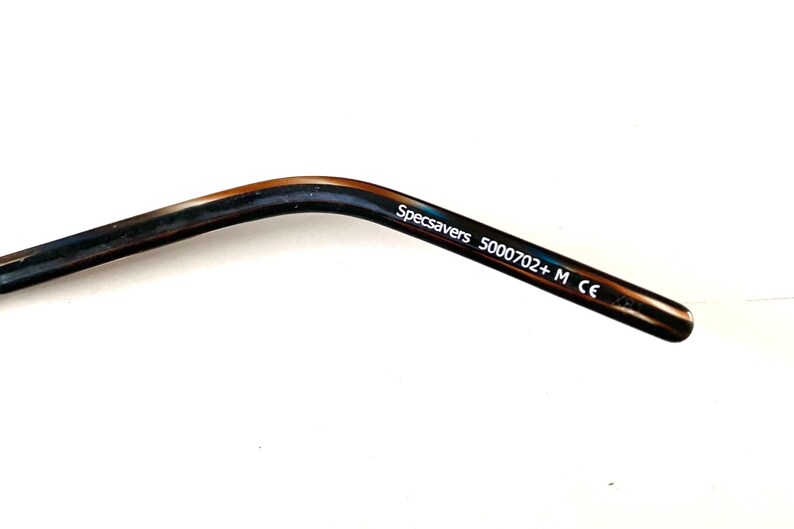 May include: Close-up of a glasses arm with a dark brown and blue marbled pattern. The text "Specsavers 5000702+ M CE" is printed in white on the arm.