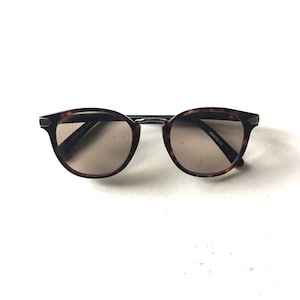 May include: Tortoise shell sunglasses with brown lenses. The sunglasses have a metal frame and the text "50052781 CE" is printed on the right lens.