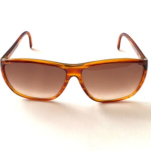 Może przedstawiać: Okulary przeciwsłoneczne w brązowej oprawie typu „żółw” z brązowymi szkłami o przejściu kolorystycznym.