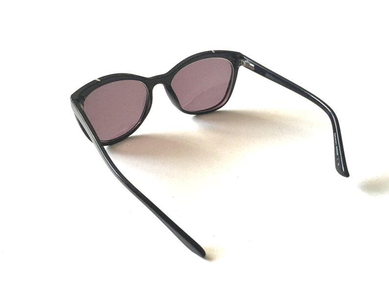 Pode incluir: &Oacute;culos de sol pretos de olho de gato com lentes escuras. Os &oacute;culos s&atilde;o de pl&aacute;stico e t&ecirc;m um design elegante e moderno.