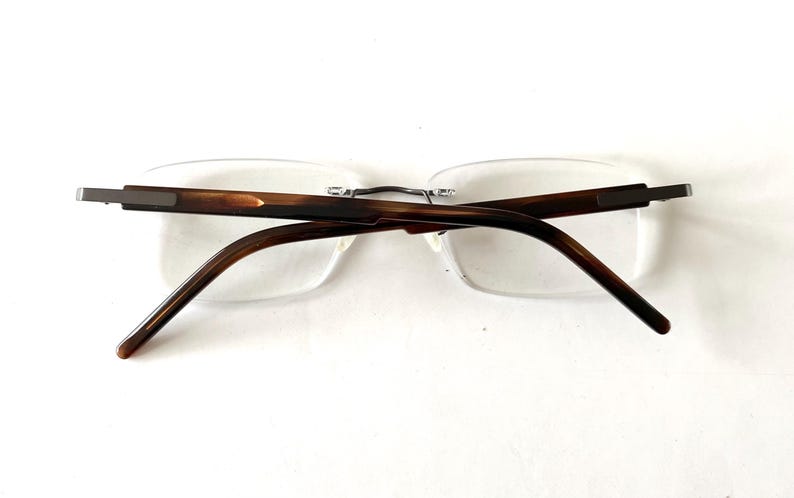 Peut inclure: Lunettes sans monture avec des branches et un pont marron et &eacute;caille de tortue. Les verres sont clairs et rectangulaires. Les lunettes sont pos&eacute;es sur un fond blanc.