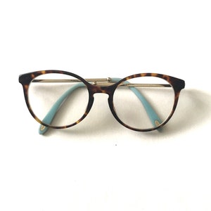 May include: Tortoiseshell eyeglasses with round frames and blue arms.