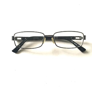 May include: Black metal rectangular frame eyeglasses with clear lenses. The frame has a subtle design detail on the temples.