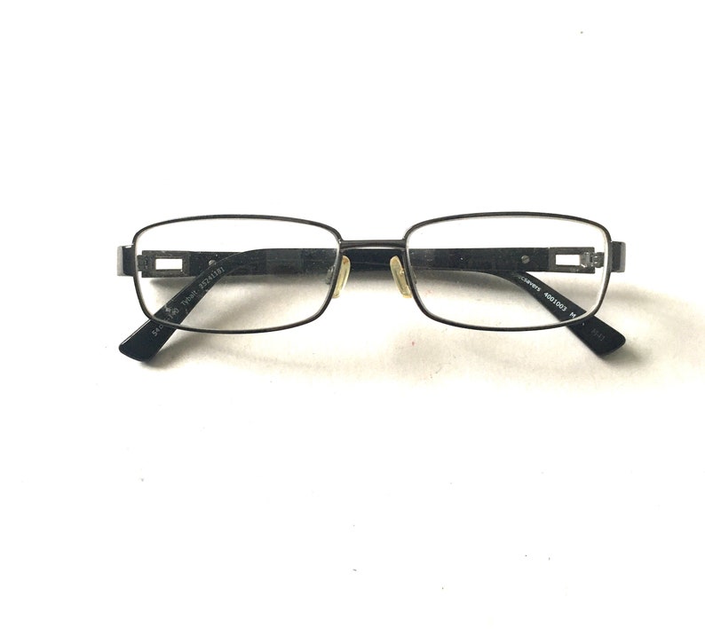 May include: Black metal rectangular frame eyeglasses with clear lenses. The frame has a subtle design detail on the temples.