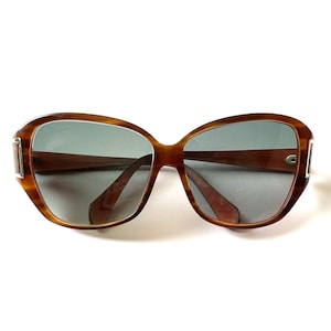 May include: Brown tortoise shell sunglasses with gray lenses. The sunglasses have a wide, rounded frame.