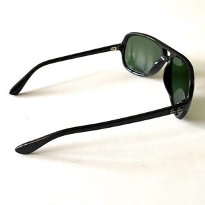 May include: Black sunglasses with green lenses. The sunglasses have a thick, rectangular frame and straight arms. The Ray-Ban logo is visible on the right arm. The lenses are a dark green color.