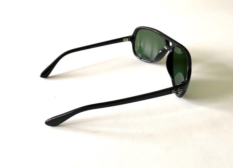 May include: Black sunglasses with green lenses. The sunglasses have a thick, rectangular frame and straight arms. The Ray-Ban logo is visible on the right arm. The lenses are a dark green color.