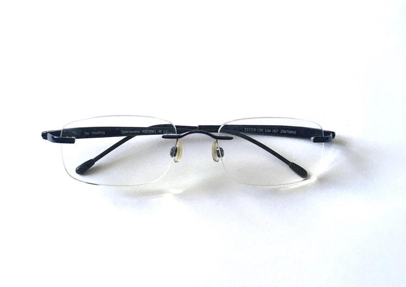 May include: Black rimless glasses with clear lenses. The glasses have a metal frame and the text "Specsavers 4903061 M CE" and "52□18-139 L167 25679942" printed on the arms.