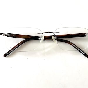 Peut inclure: Lunettes sans monture avec des branches &agrave; motifs marron et noir et un fin pont en m&eacute;tal fonc&eacute;. Les verres sont rectangulaires et transparents. Le texte sur la branche indique "53016-135 Lite 177 3004102".