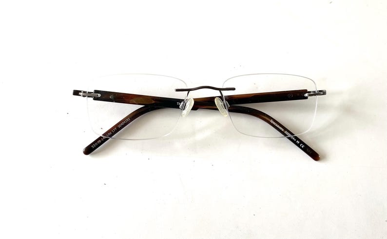 Peut inclure: Lunettes sans monture avec des branches &agrave; motifs marron et noir et un fin pont en m&eacute;tal fonc&eacute;. Les verres sont rectangulaires et transparents. Le texte sur la branche indique "53016-135 Lite 177 3004102".