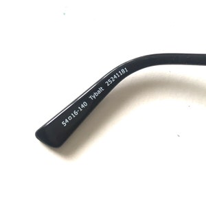 May include: Close-up of the black arm of a pair of glasses with the text "54□16-140 Tybalt 25241181" printed on the inside.