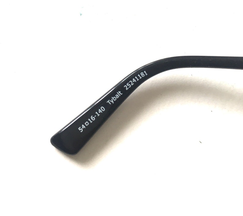 May include: Close-up of the black arm of a pair of glasses with the text "54□16-140 Tybalt 25241181" printed on the inside.