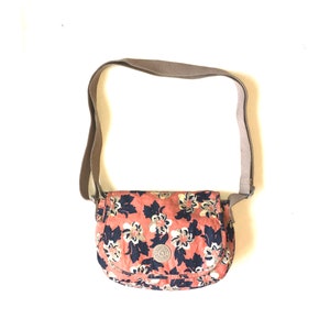 May include: A brown and beige floral patterned crossbody bag with a brown strap. The bag has a small logo on the front.